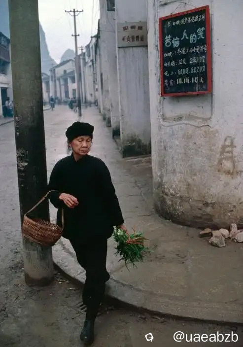 1980年的桂林，由法国摄影家布鲁诺·巴贝拍摄，阳朔的一处街头，一位大妈一手挎着篮子，一手拿着蔬菜走过， ...