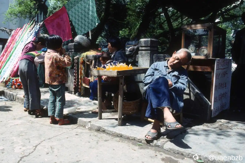 1988年的桂林，由外国摄影人Paolo Vieceli拍摄，在临街的一处石桥旁，栏杆处摆着几个摊位，睡觉的老汉是维 ...